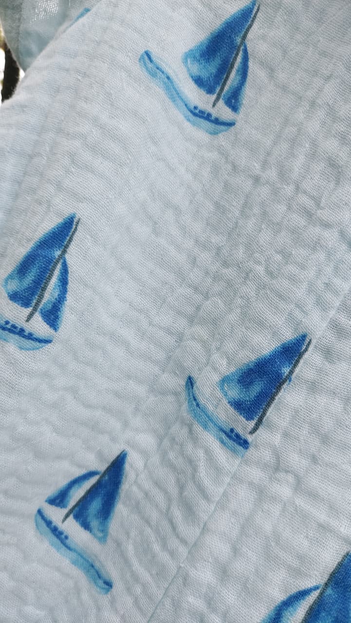 A close-up of a light gray quilted fabric featuring a repeating pattern of blue and navy sailboats.