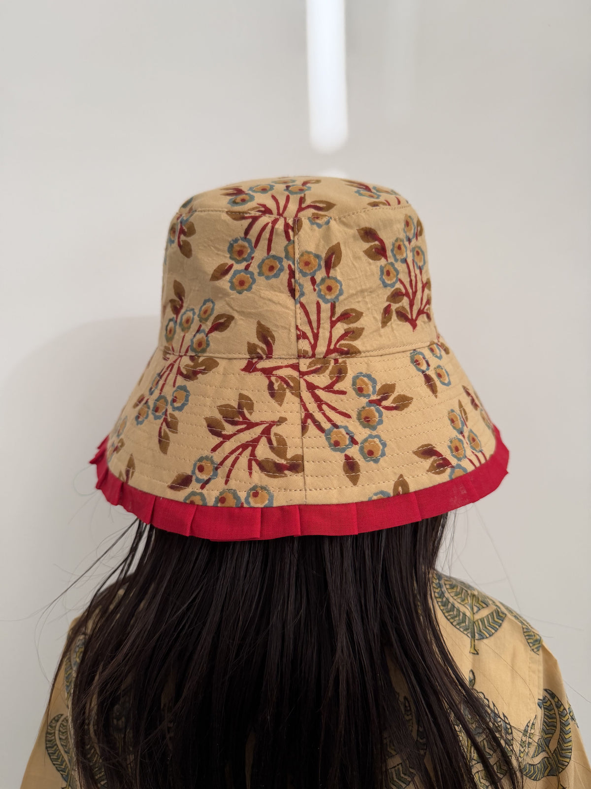 Person wearing a beige bucket hat with floral patterns and red trim against a white background