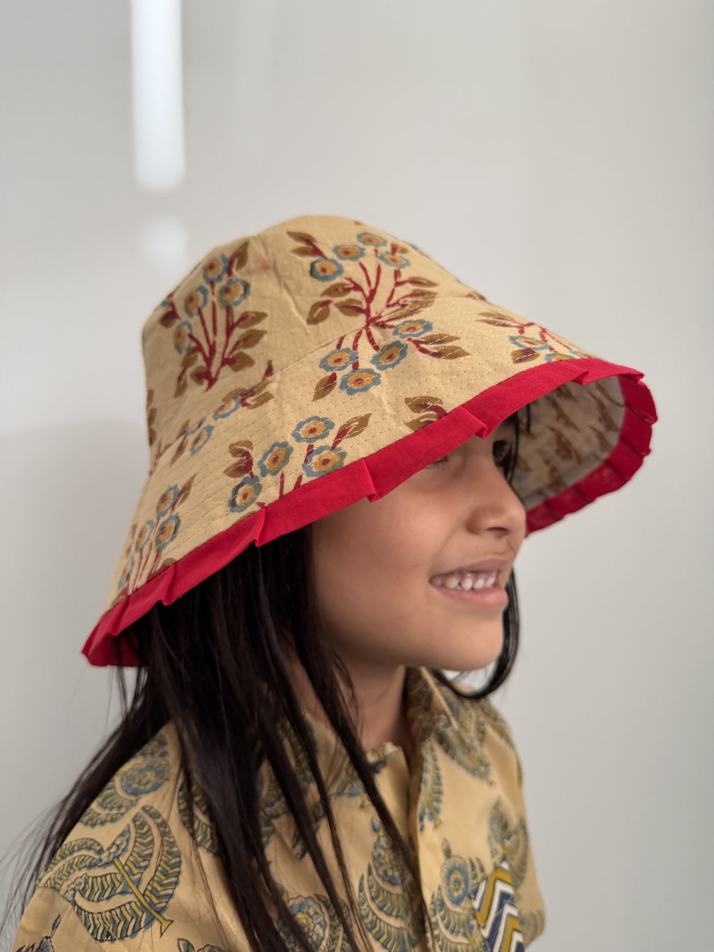 Child wearing a floral-patterned hood with red trim on a plain background