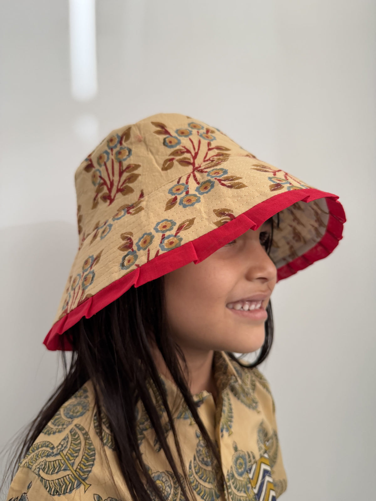 Child wearing a floral-patterned hood with red trim on a plain background