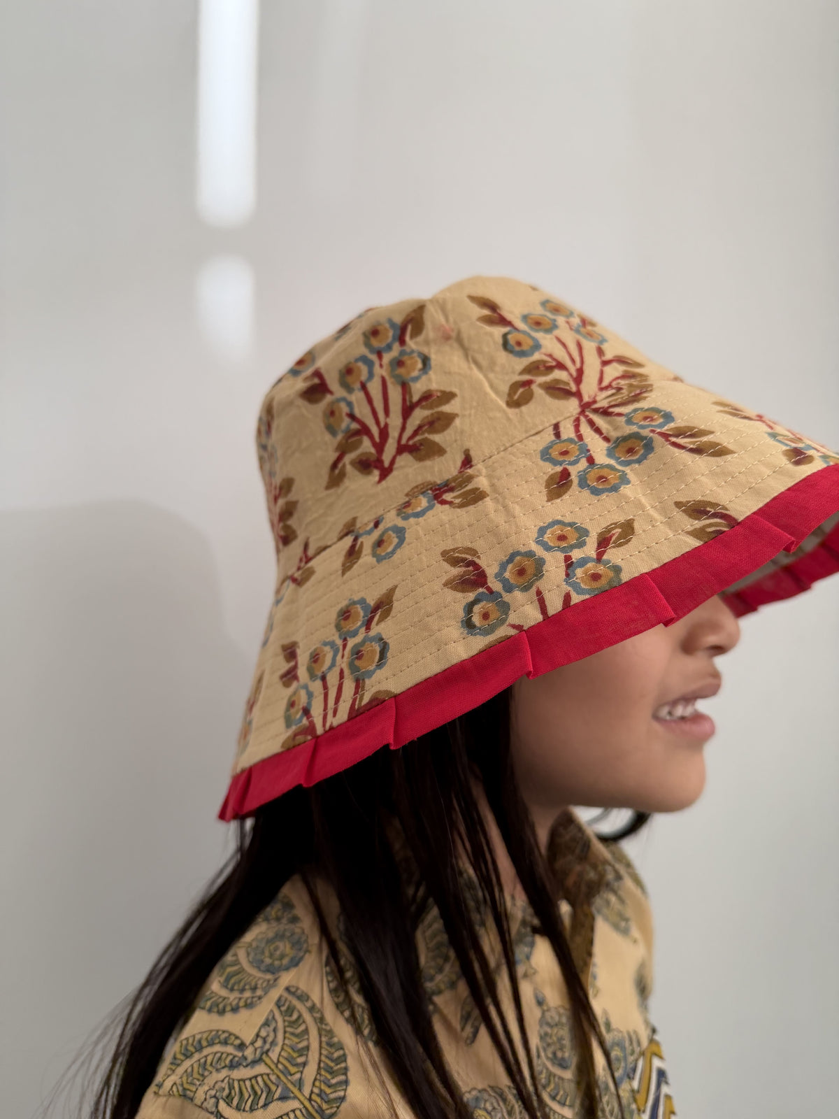 Person wearing a floral-patterned hat with red trim against a plain background