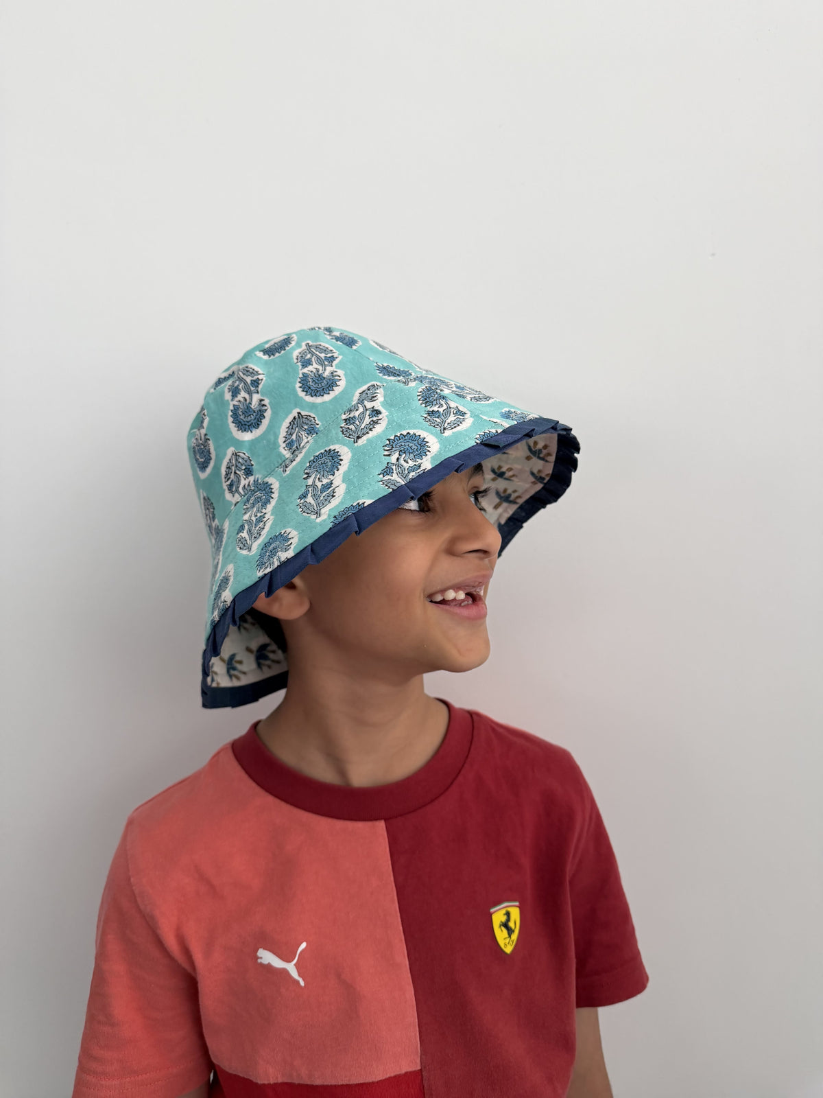 Child wearing a patterned hat and a red shirt with a logo on a plain background