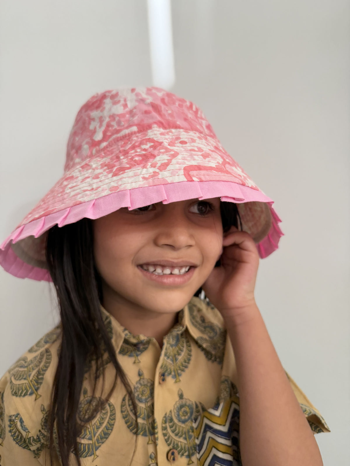 Child wearing a pink patterned hat and a yellow dress with a white background
