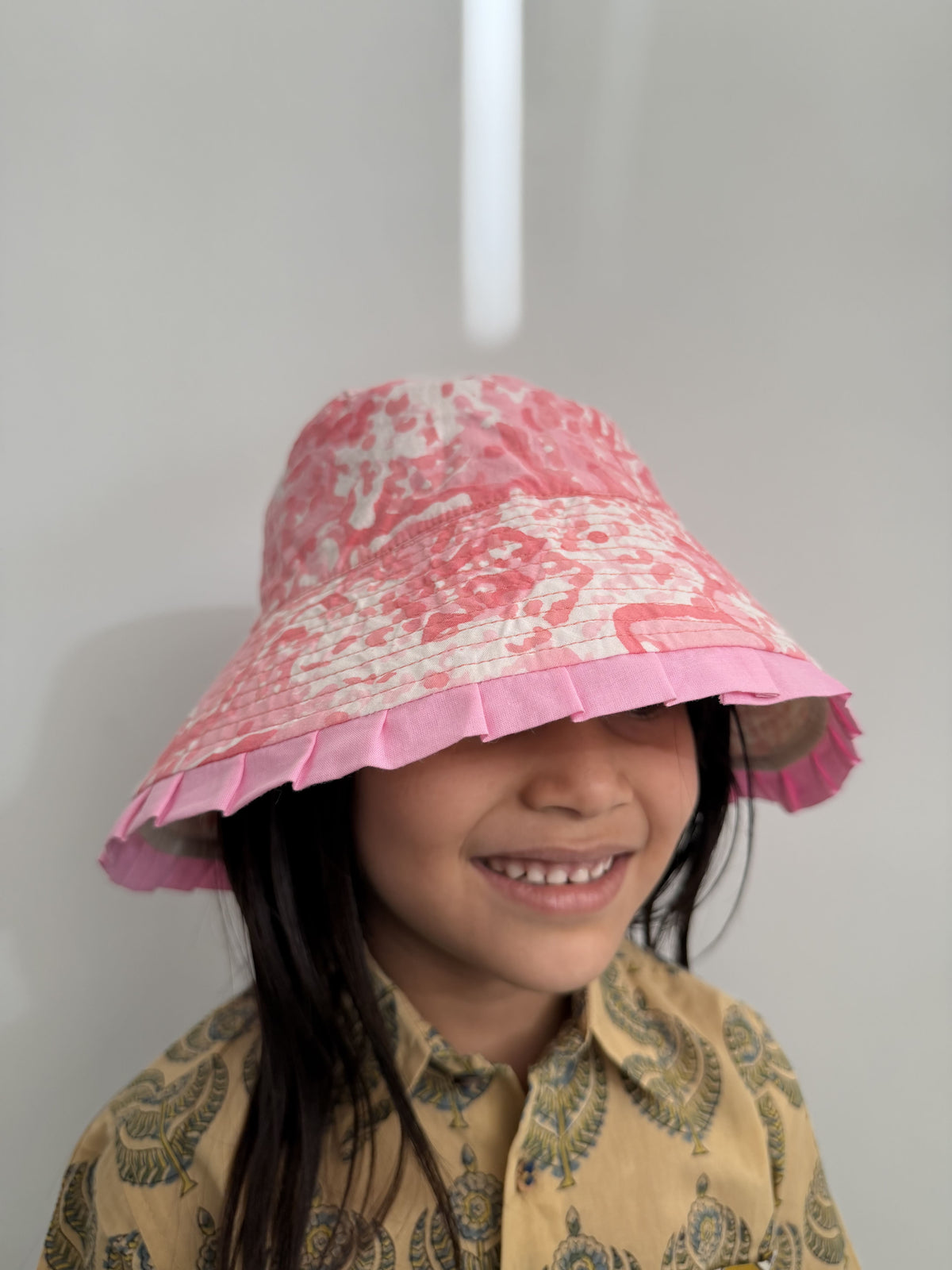 Person wearing a pink patterned hat and a yellow patterned coat on a white background