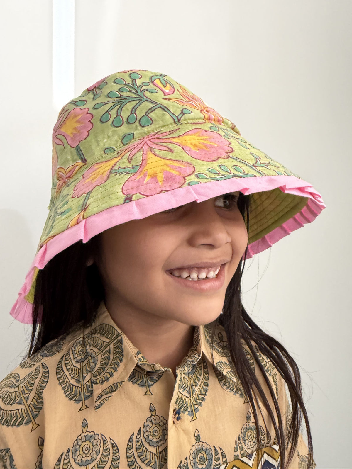 Child wearing a colorful floral bucket hat with pink trim against a white background