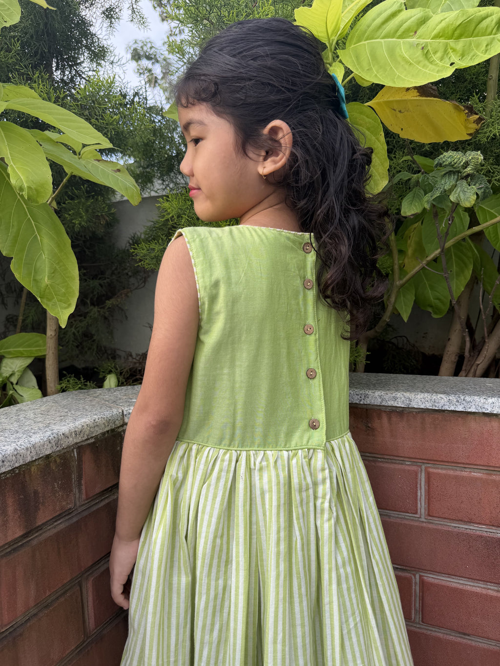 A girl wearing a dress with wooden button on it and she is wearing a smocking dress