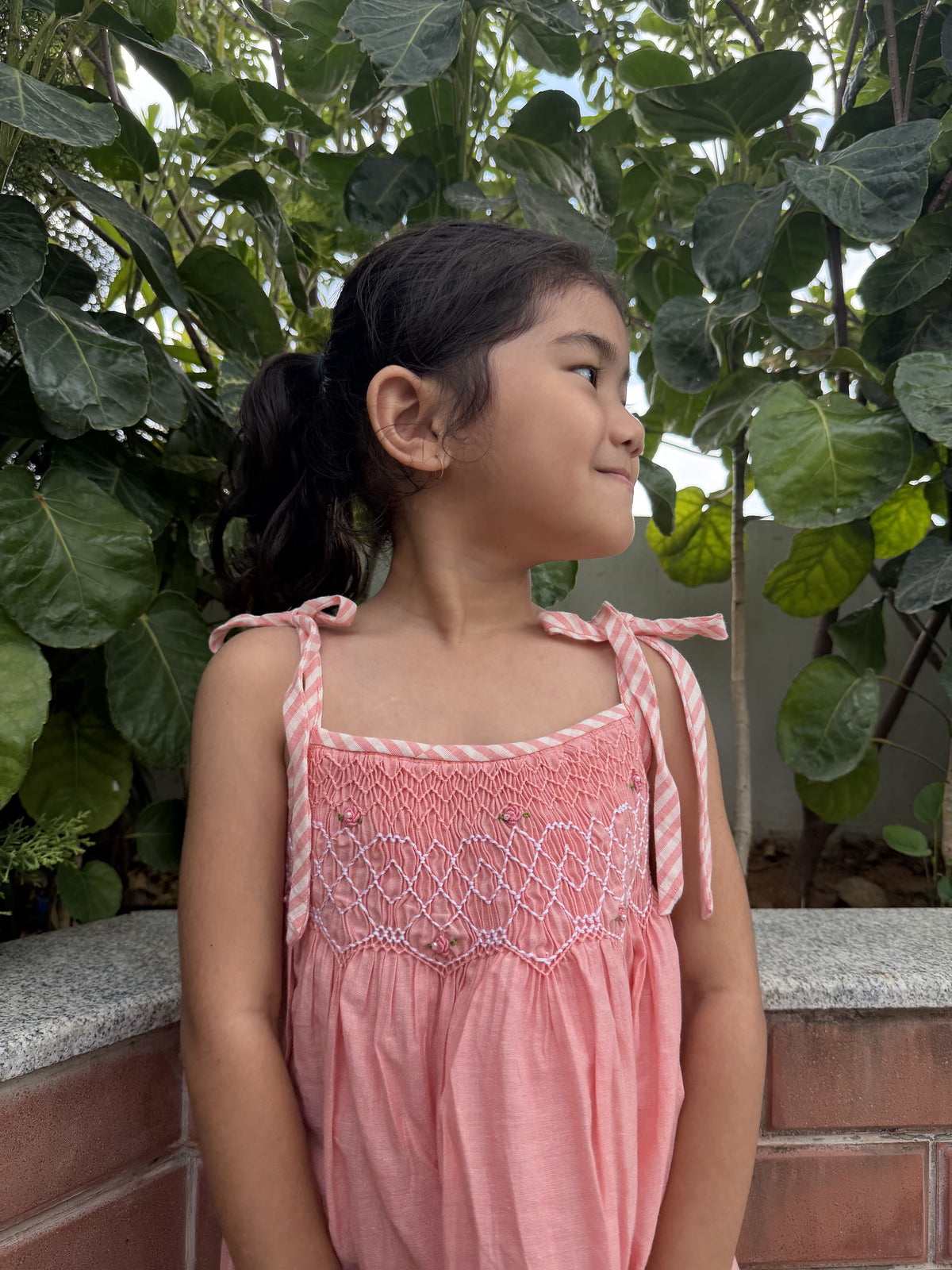 Woman in a pink dress standing outdoors with greenery around