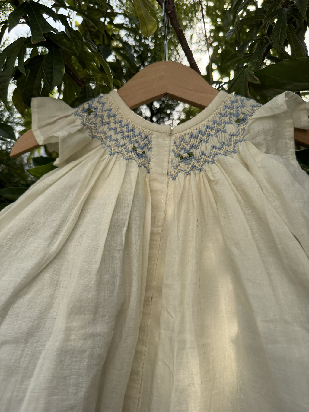 Close-up of a white dress with blue embroidery against a blurred natural background