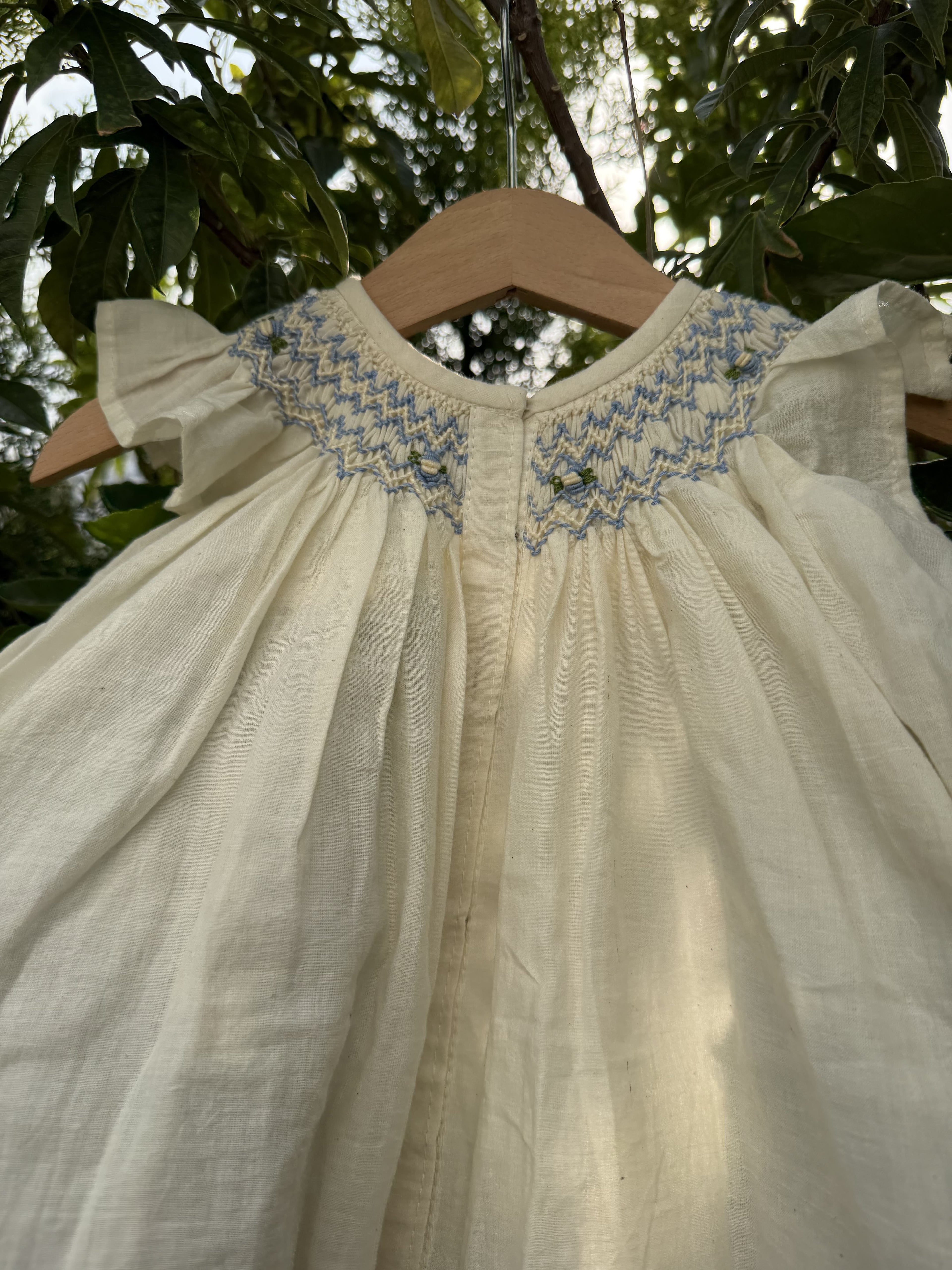 Close-up of a white dress with blue embroidery against a blurred natural background