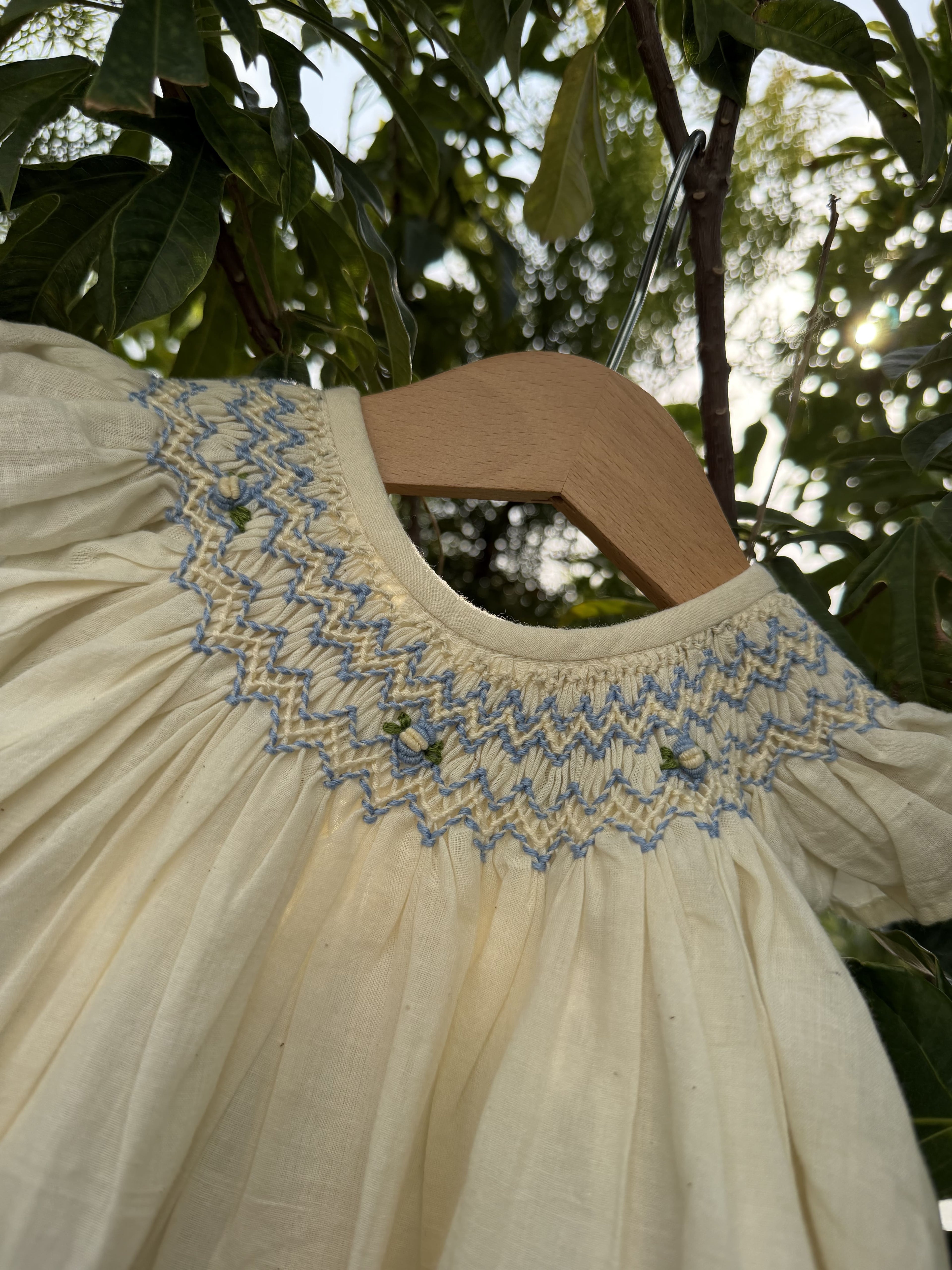 Beige dress with blue embroidery on a hanger against a natural background