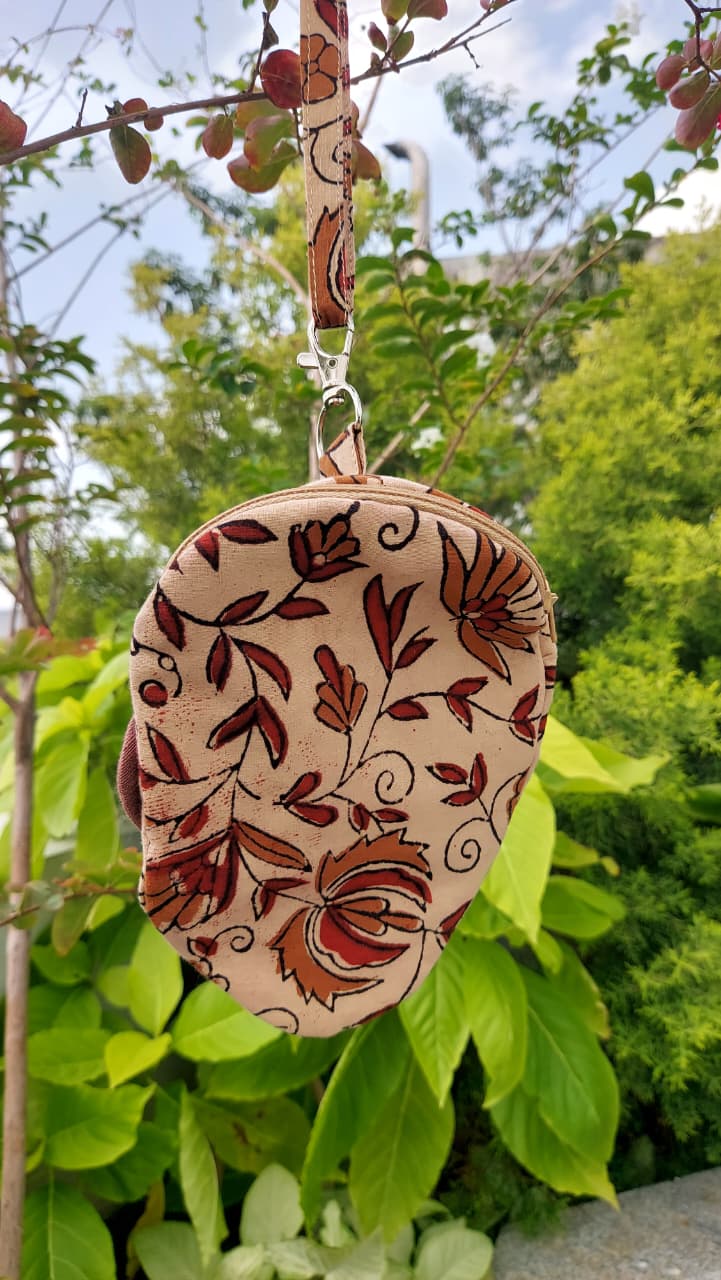 A small fabric pouch with a floral pattern hanging from a tree branch outdoors, surrounded by green leaves and foliage.